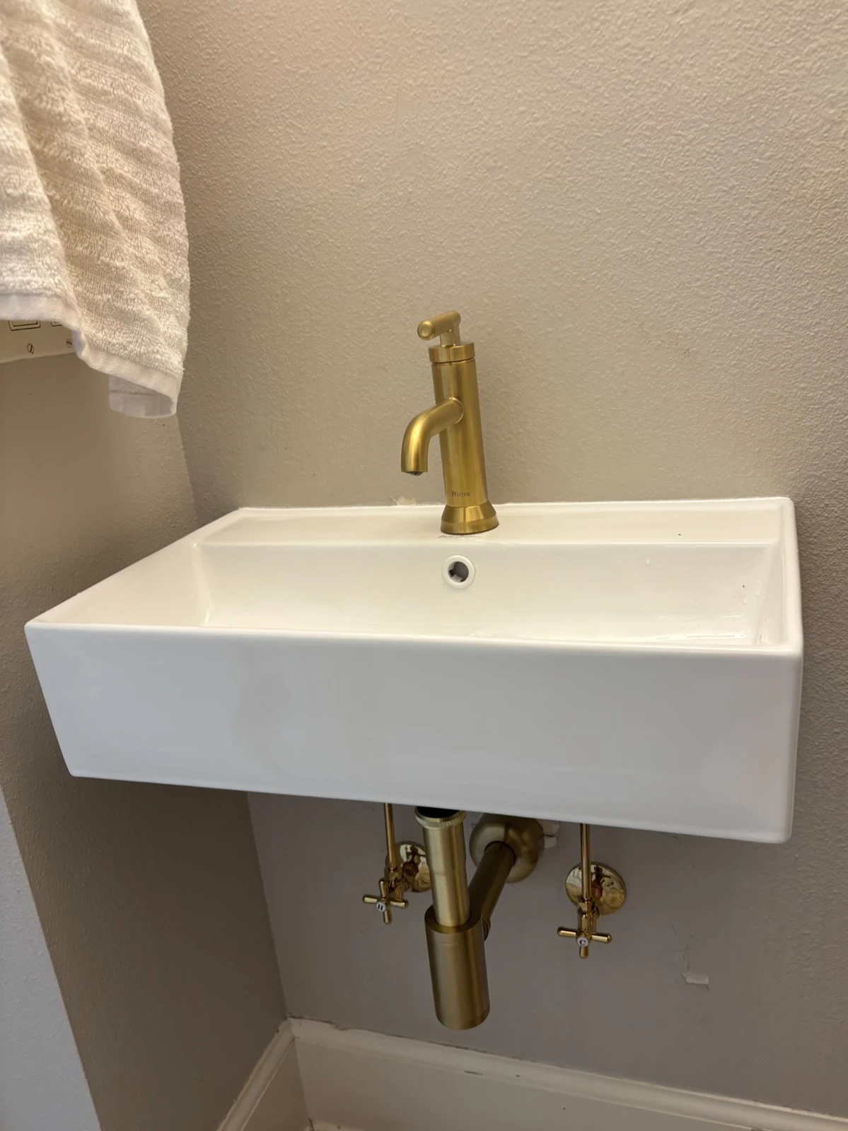 White wall-mounted sink with a brass faucet, drain, and exposed connections