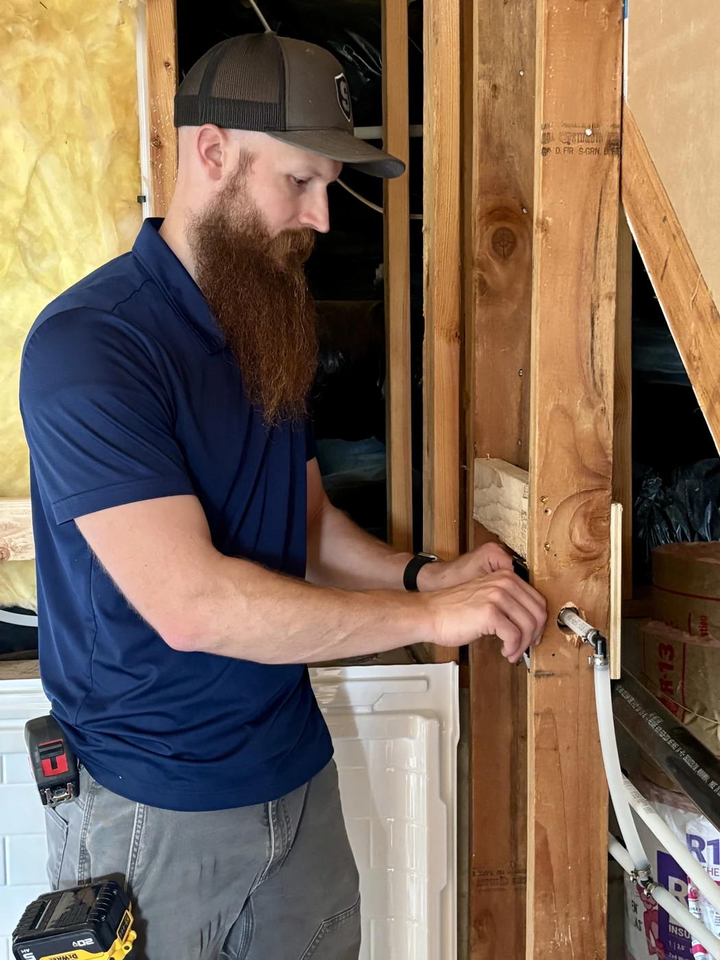 Will Mortensen working on a water connection beside exposed framing during a bathroom remodel